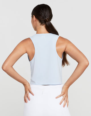 Woman wearing a light blue sleeveless top and white pants on a plain background