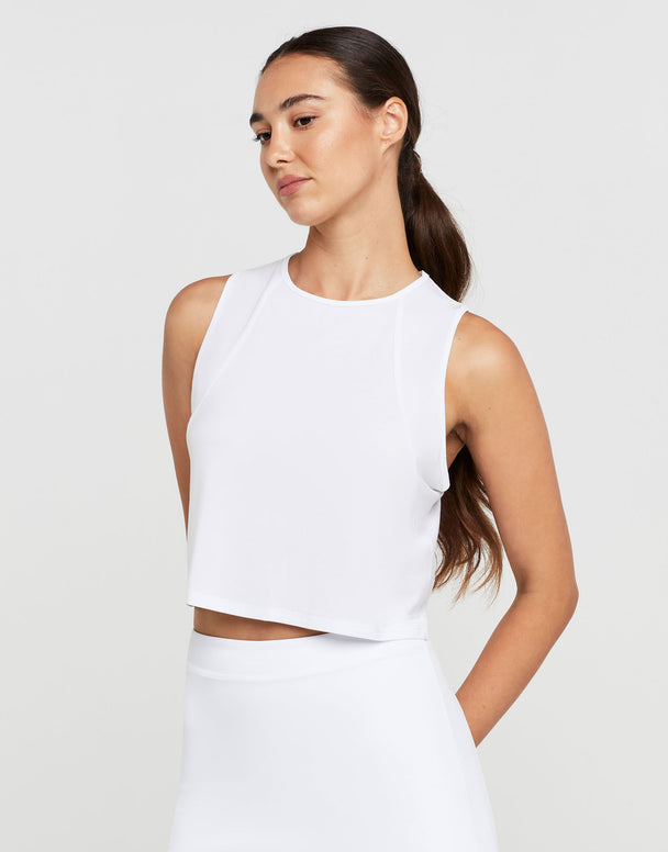 Woman wearing a white sleeveless top and pants on a plain background