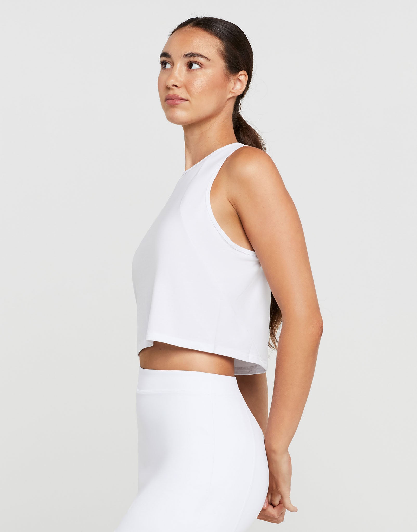 Woman wearing a white sleeveless top and pants on a light gray background