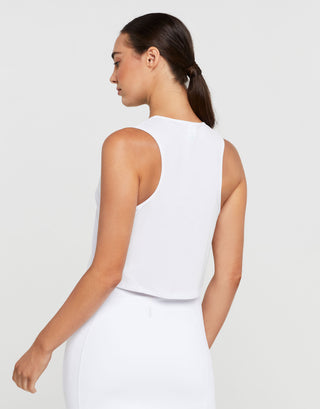 Woman wearing a white sleeveless top and pants on a plain background