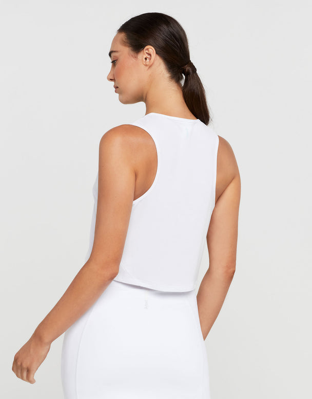 Woman wearing a white sleeveless top and pants on a plain background