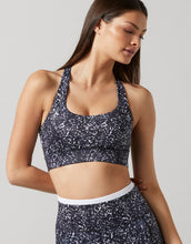 A woman wearing a black and white speckled sports bra with thick straps, paired with a matching crop top.