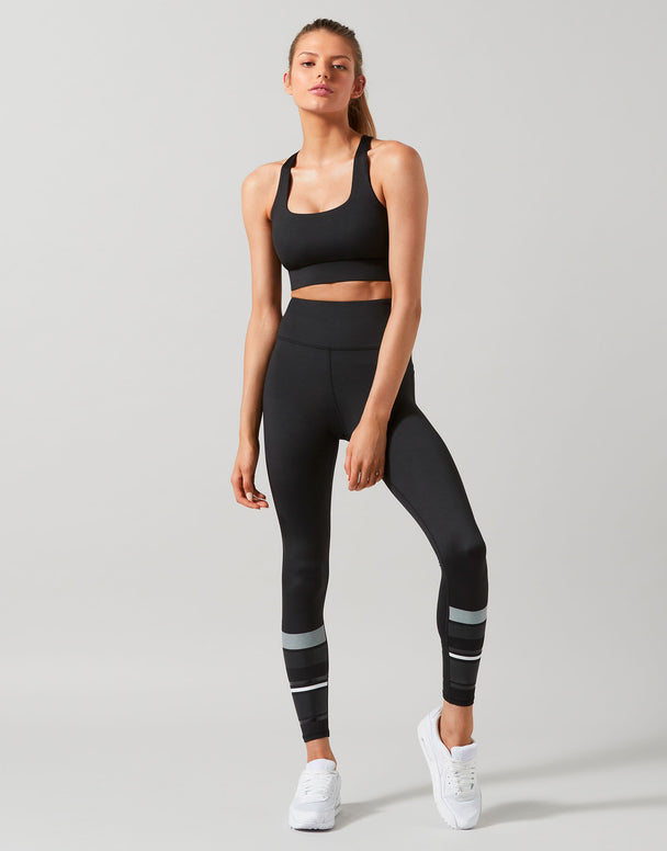 Woman wearing a black athletic outfit with reflective stripes on a gray background