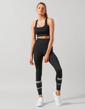 Woman wearing a black athletic outfit with reflective stripes on a gray background