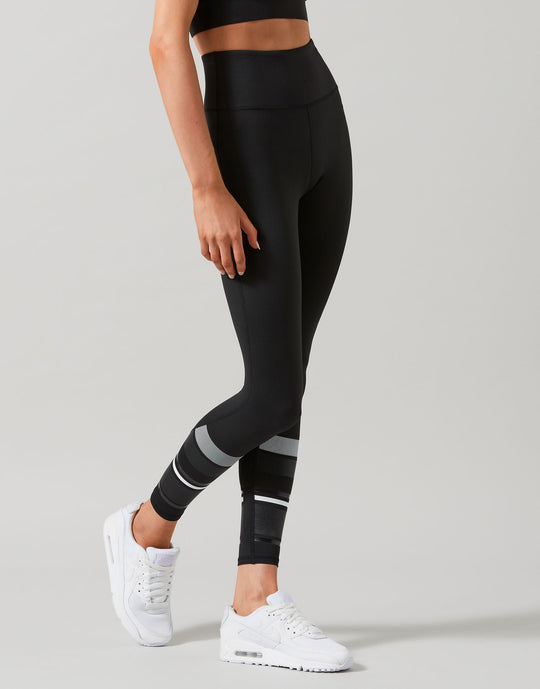 Person wearing black leggings with white stripes on a gray background