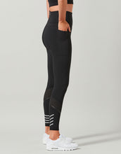 Person wearing black athletic leggings with white stripes on a gray background