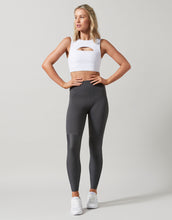 Woman wearing a white crop top and dark gray leggings on a light gray background