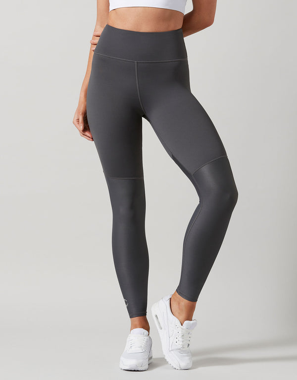 Person wearing dark gray leggings with white sneakers on a light gray background