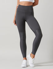 Person wearing dark gray leggings with white sneakers on a light gray background