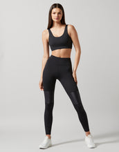 A model wearing black high-waisted leggings with a full-length design. The person is also wearing a sports bra and white sneakers.