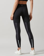 A person standing and facing away wearing black high-waisted leggings with a full-length design. The person is also wearing a sports bra and white sneakers.