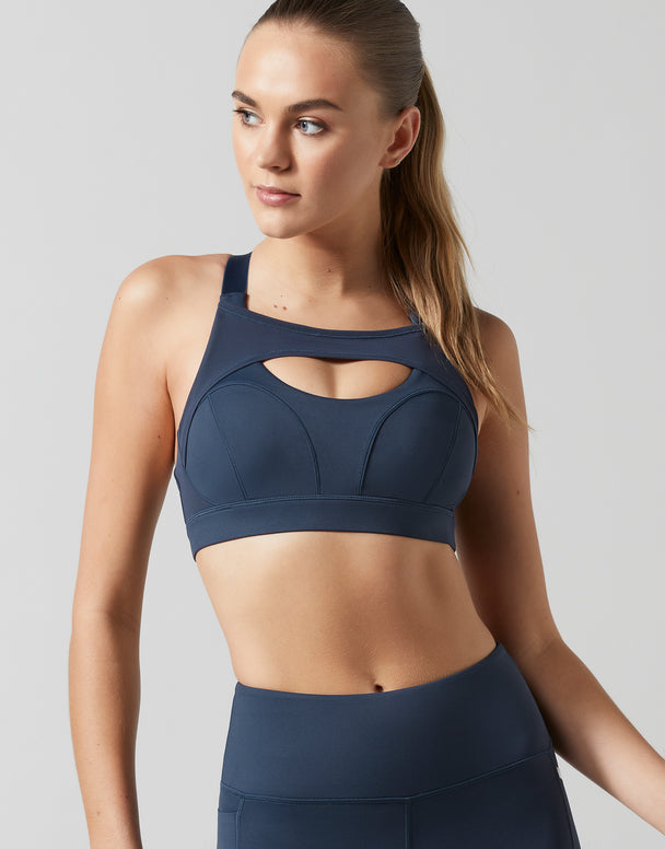 Woman wearing a navy blue sports bra and leggings on a light gray background