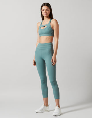 Woman wearing a teal sports bra and leggings set on a light gray background