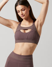 Woman wearing a brown sports bra and leggings against a light gray background