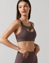 Woman wearing a brown sports bra and leggings on a light gray background
