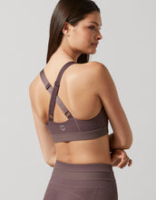 Woman wearing a brown sports bra and leggings on a light gray background