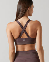 Woman wearing a brown sports bra and leggings on a plain background