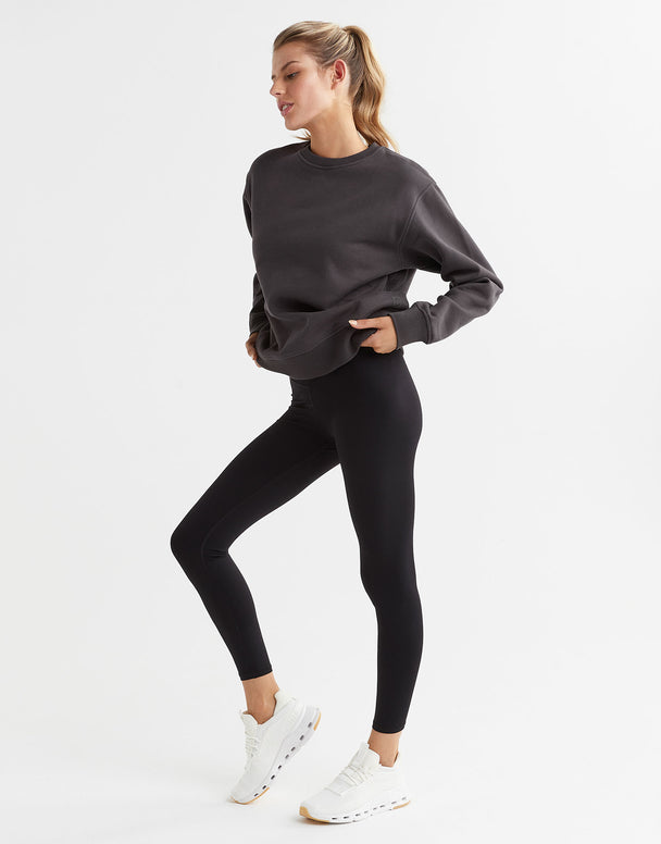 A female model wearing a gray Lilybod Montana fleece crew sweater, which is designed with a crew neck and long sleeves and leggings.
