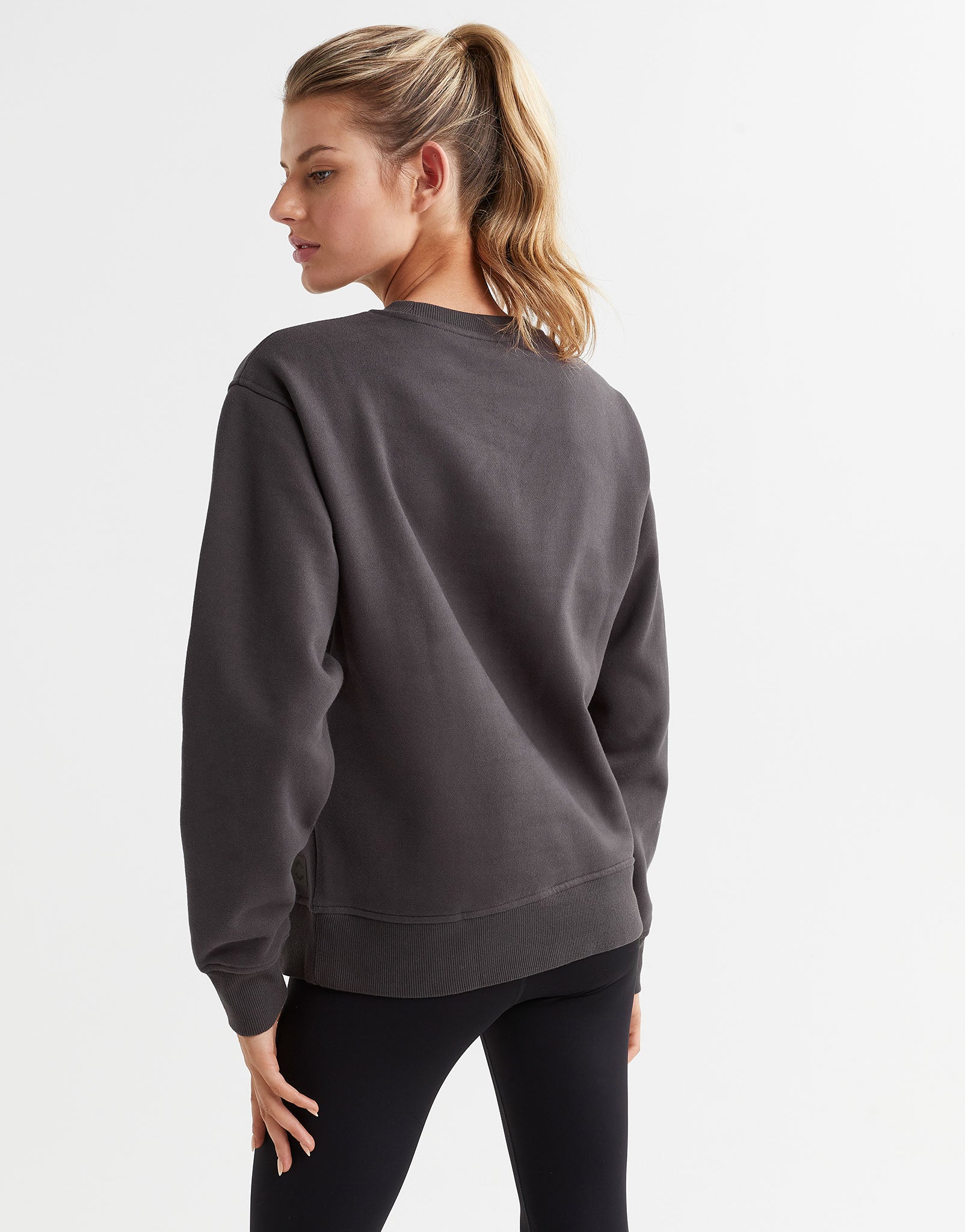 A female model wearing a gray Lilybod Montana fleece crew sweater, which is designed with a crew neck and long sleeves with black leggings.