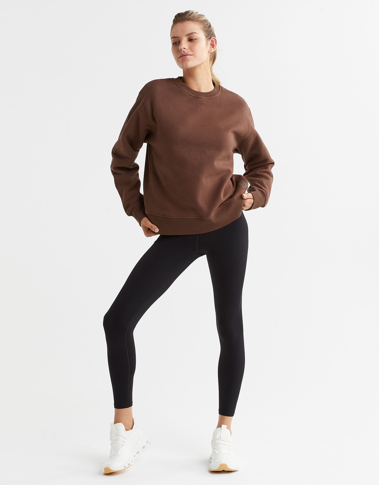 A model wearing a brown crew neck fleece crew sweater with elasticised cuffs and a Lilybod accent logo on the front and leggings.