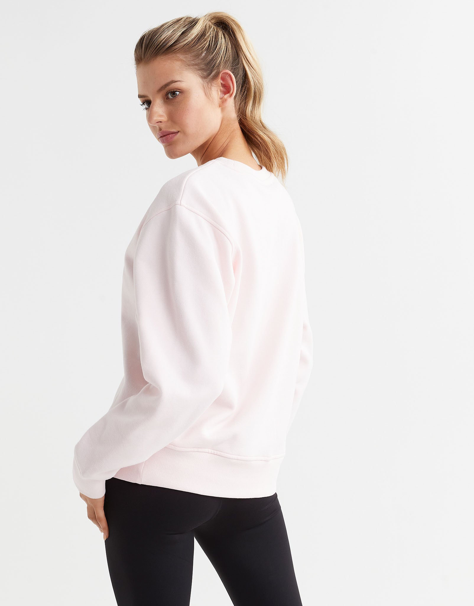 A woman wearing a light pink crew neck sweater and black leggings.