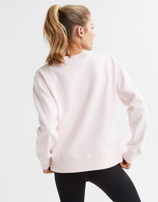 A woman wearing a light pink crew neck  fleece sweater and black leggings.