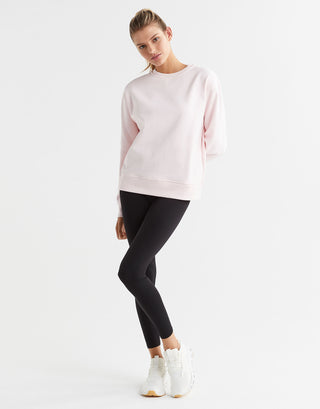 A woman wearing a light pink crew neck sweater and black leggings with white runners.