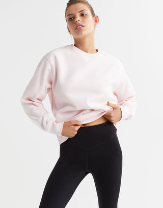 A model wearing a light pink crew neck sweater and black leggings.