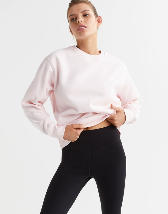 A model wearing a light pink crew neck sweater and black leggings.