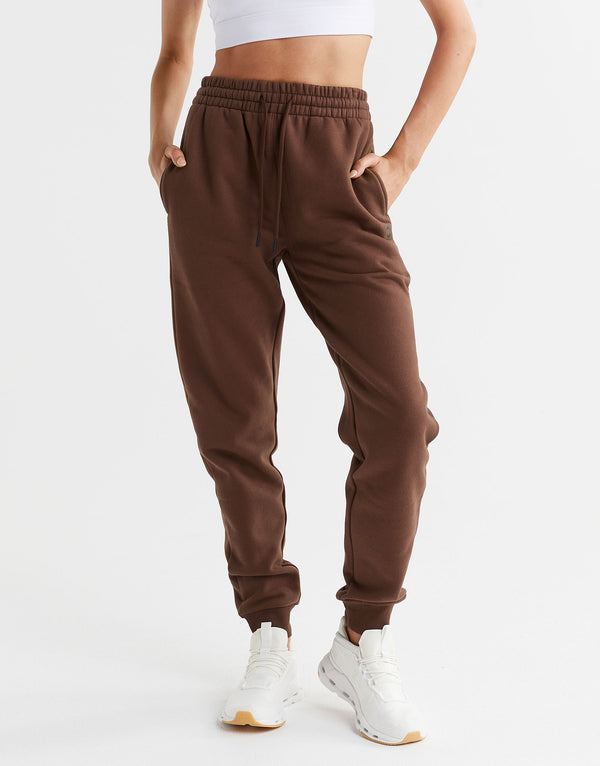 A model wearing brown track pants a white top and white sneakers.