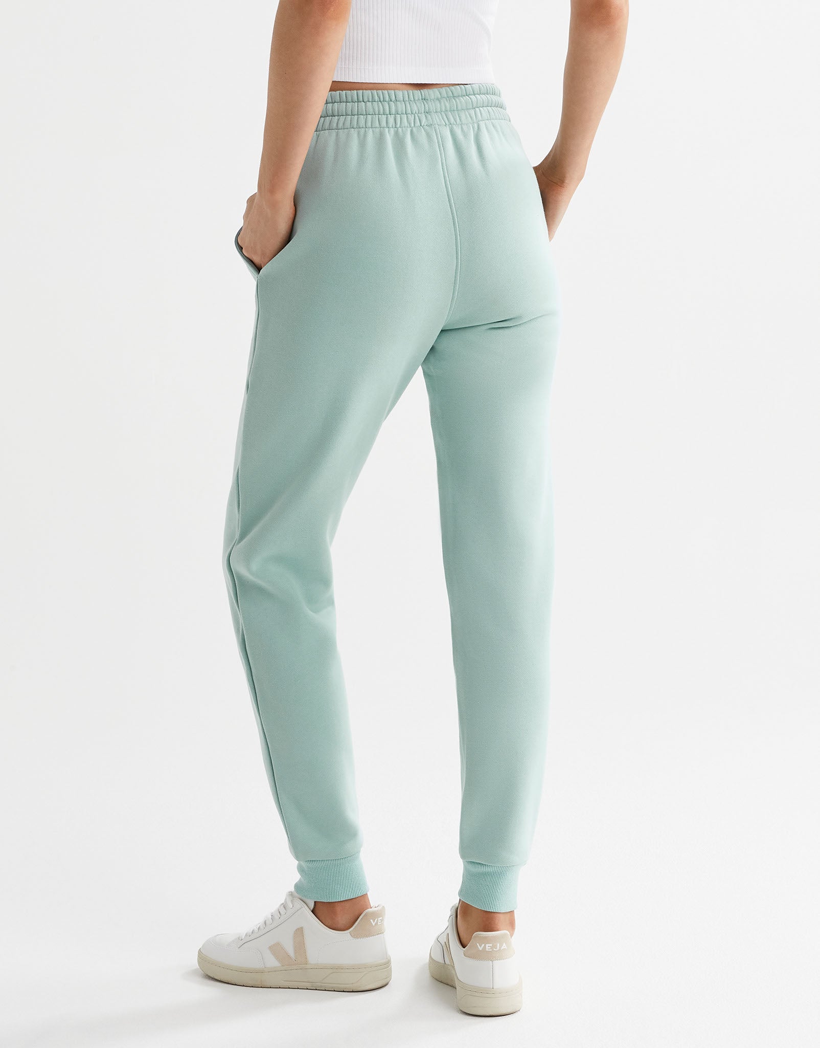 A pair of sage green fleece-lined slim leg sweatpants with a drawstring waistband, pockets, and lilybod accent details and white runners.