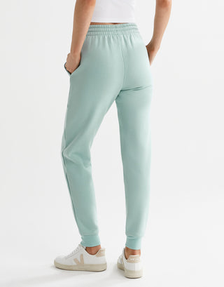 A pair of sage green fleece-lined slim leg sweatpants with a drawstring waistband, pockets, and lilybod accent details and white runners.
