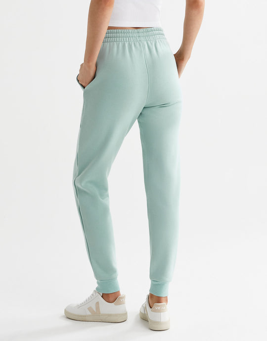 A pair of sage green fleece-lined slim leg sweatpants with a drawstring waistband, pockets, and lilybod accent details and white runners.