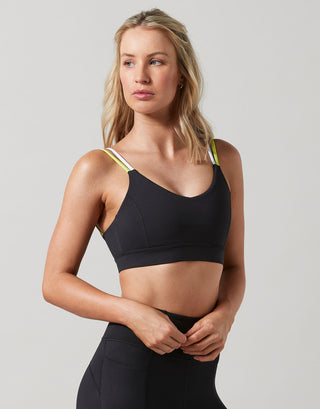 Woman wearing a black sports bra with green straps on a light gray background