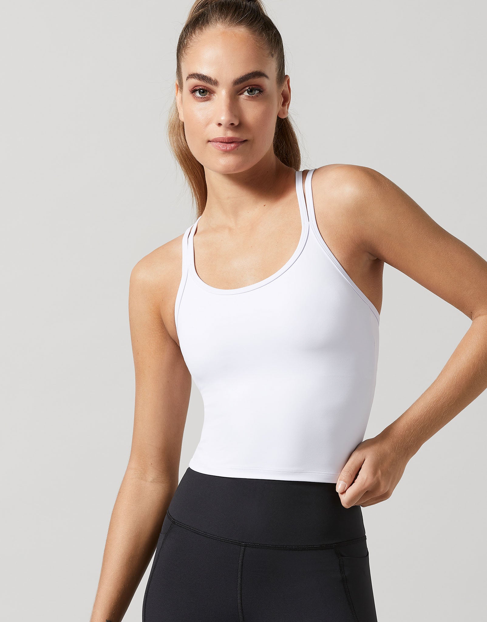 A woman wearing a white sports bra top and black activewear pants.