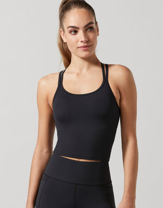 A woman wearing a black strappy activewear top and black leggings.