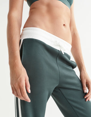 Person wearing green athletic pants with a white waistband on a light gray background