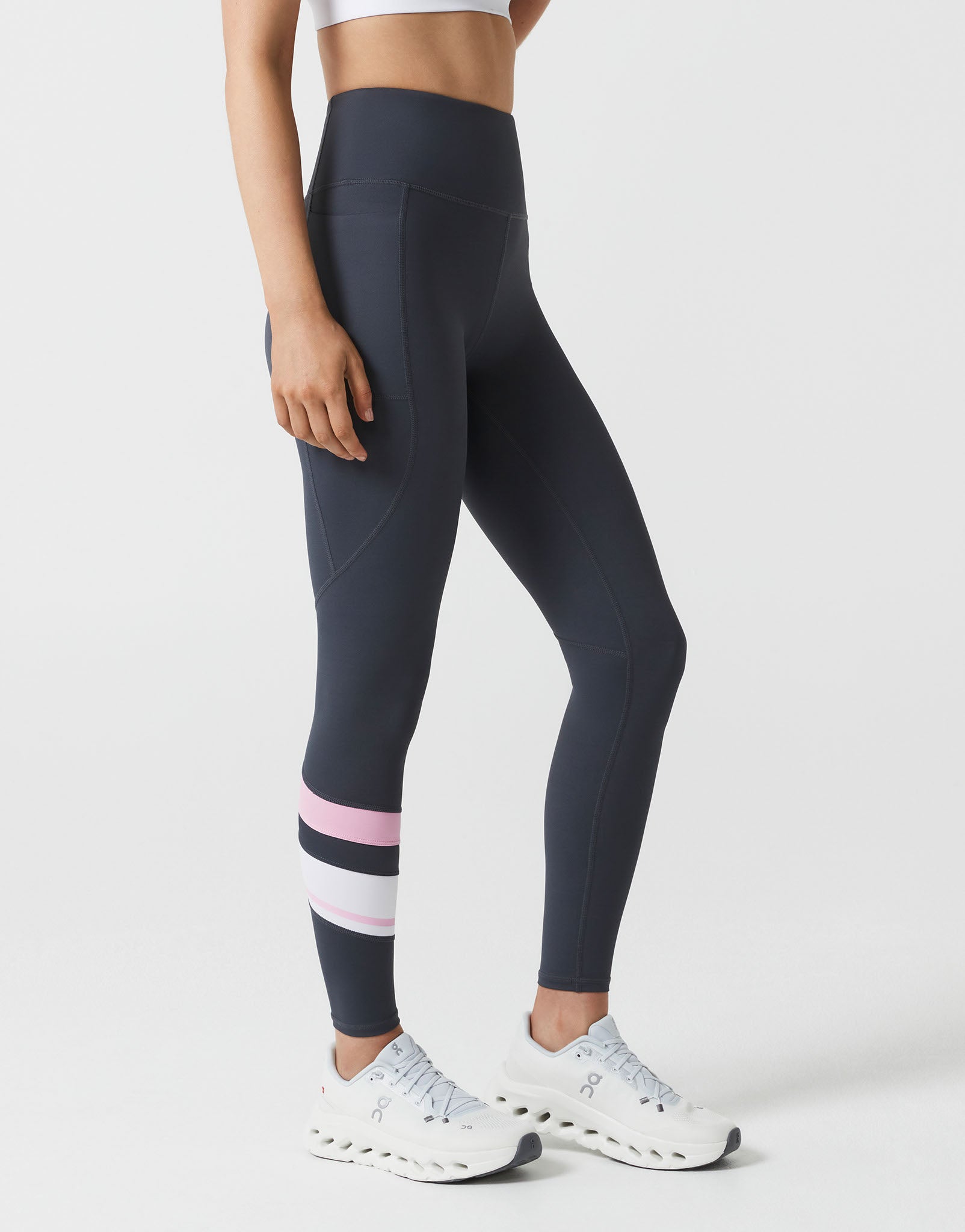 Person wearing navy leggings with pink stripes and white sneakers on a light gray background