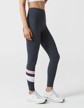 Person wearing navy leggings with pink stripes and white sneakers on a light gray background