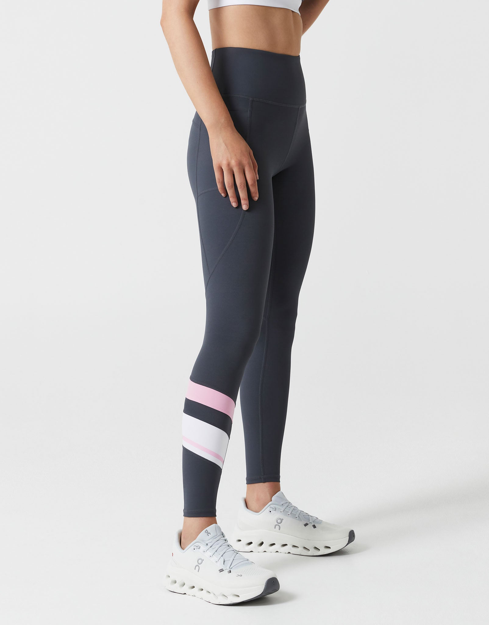 Person wearing dark gray leggings with pink and white striped socks on a light gray background