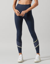Person wearing navy leggings with white and yellow accents on a gray background