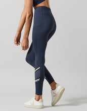 A woman wearing navy full-length leggings with contrasting white, blue nights, and yellow lemon accents. The leggings have a high-waist fit and feature a phone pocket.