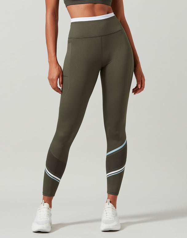 Person wearing olive green leggings with white accents on a light gray background