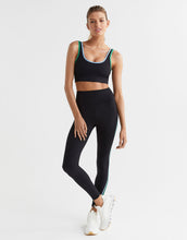 Woman wearing a black sports bra and leggings with green accents on a white background