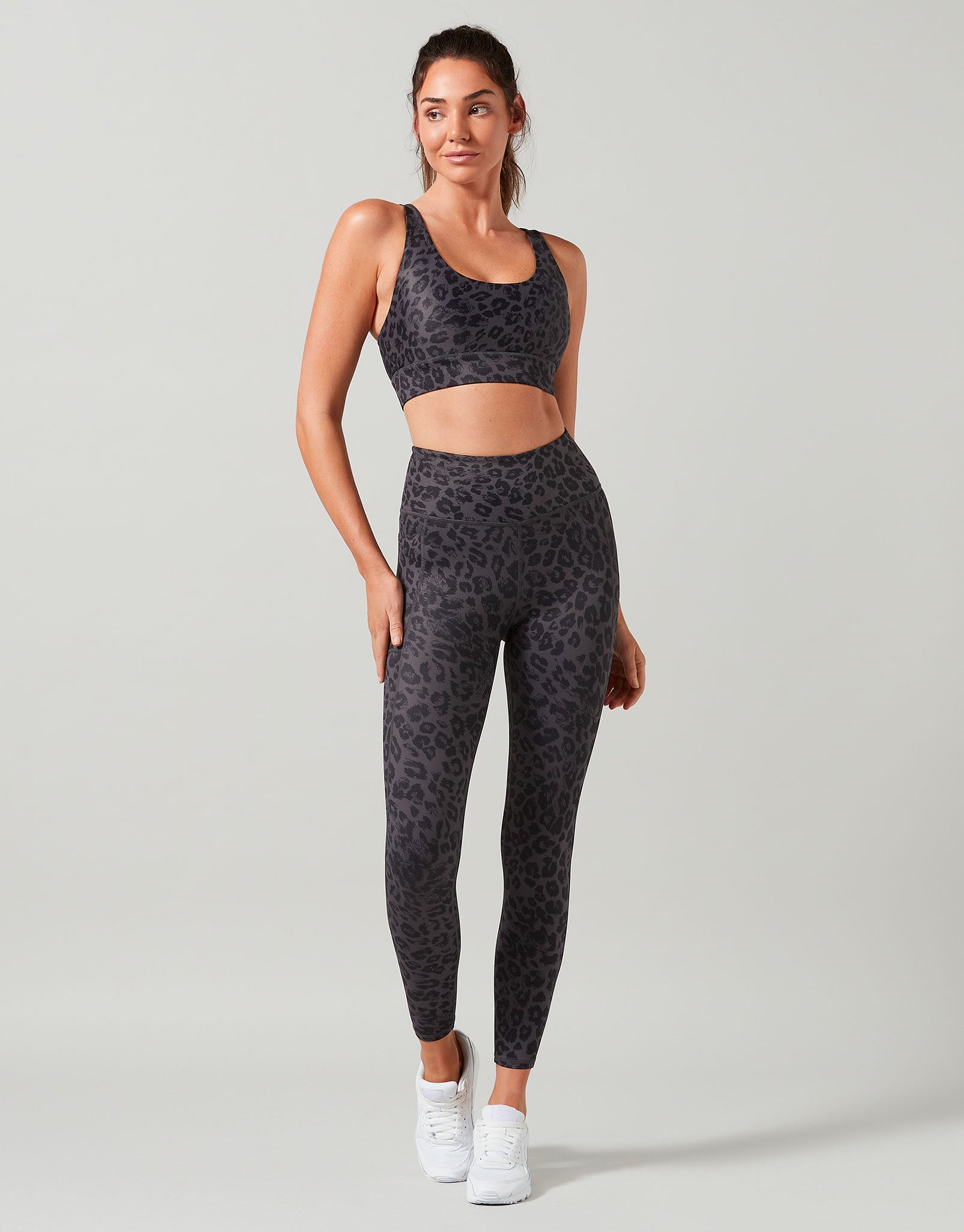 A woman wearing a leopard print sports bra and leggings with a scooped neckline, wide adjustable straps, and an open back design.