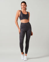 Woman wearing a black leopard print sports bra and leggings set on a gray background