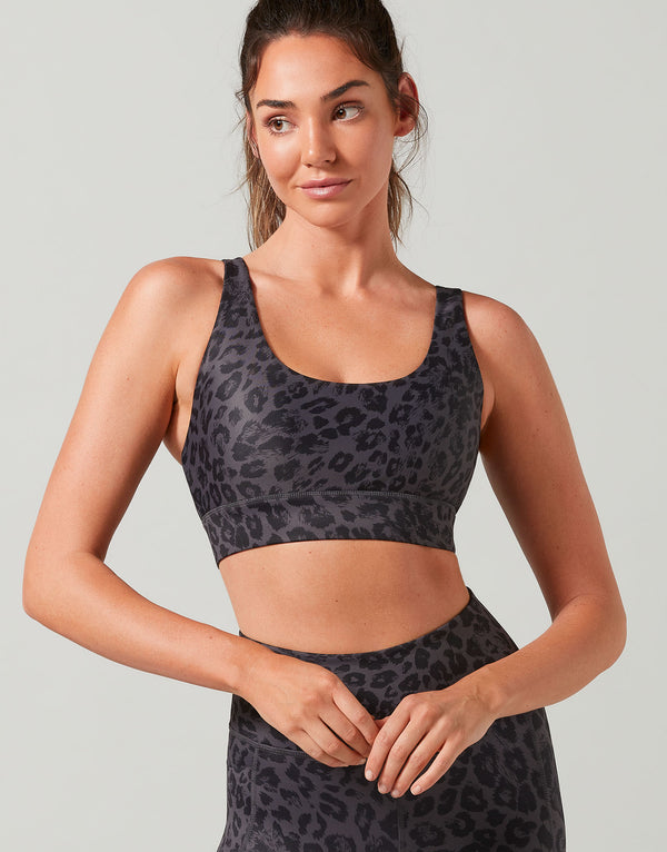 Woman wearing a black leopard print sports bra and leggings on a light gray background