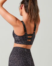 Person wearing a black leopard print sports bra and leggings on a light gray background