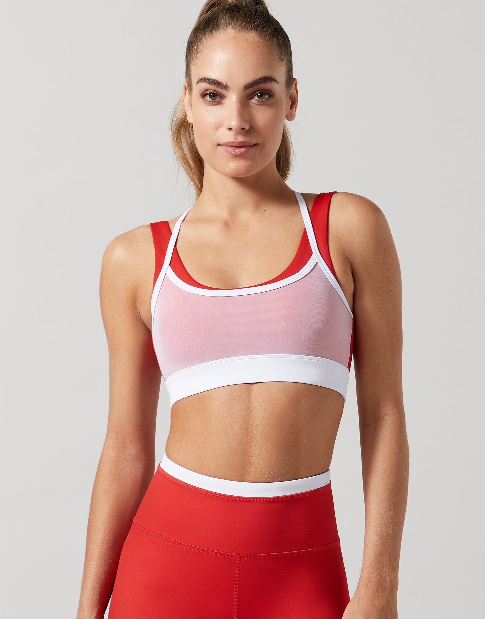 A woman wearing a red and white double layer sports bra with red leggings with white details.