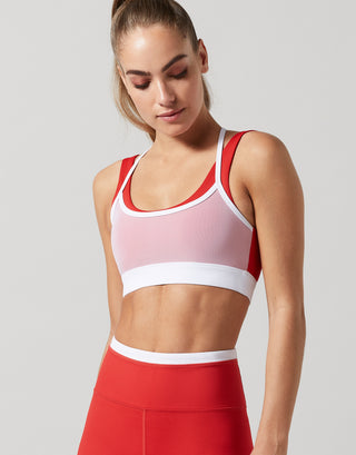 A model wearing a red and white double layer sports bra with red leggings.